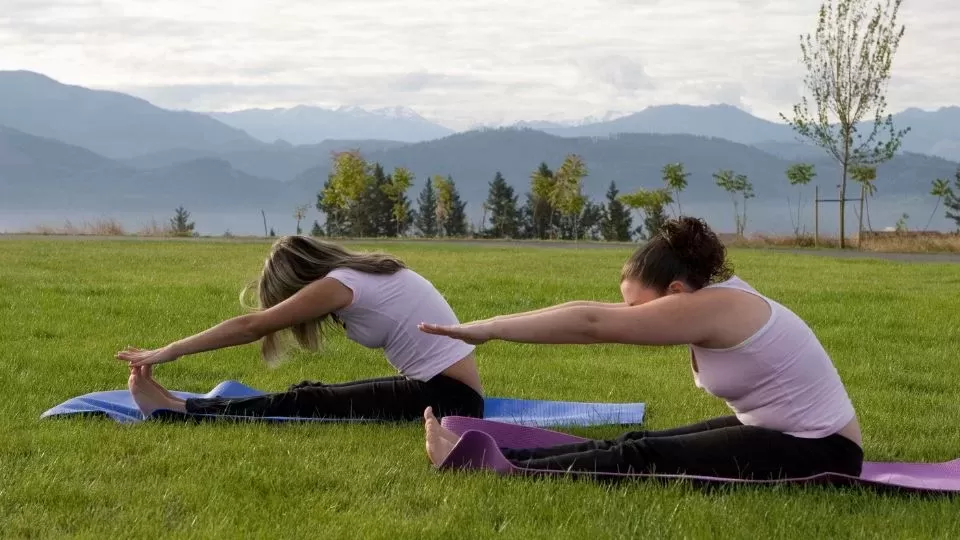 Two Women Stretching Legs And Practicing Yoga In Garden