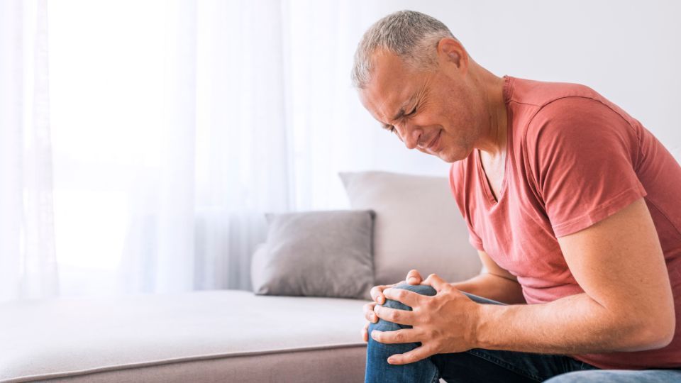 Man Suffering From Knee Pain Sitting On Couch