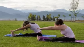 Two Women Stretching Legs And Practicing Yoga In Garden